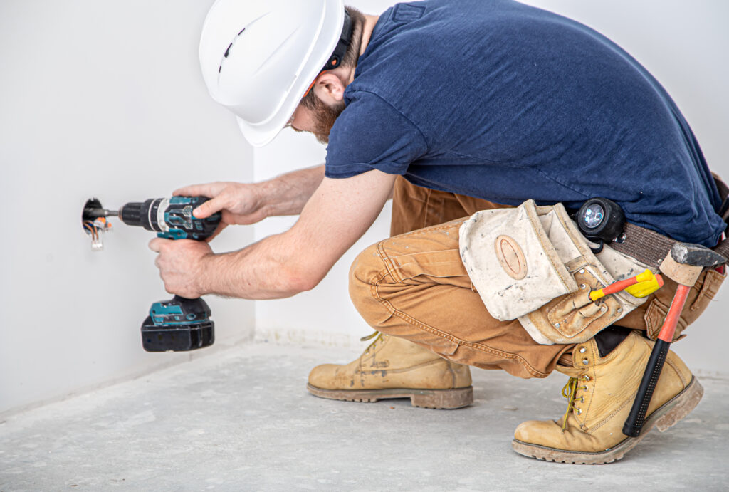 electrician builder in a white helmet with a drill, installation of sockets, and switches close up.